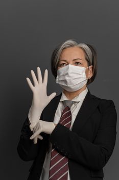 Caucasian Businesswoman in protective mask put on disposable gloves. Mature female office worker puts on protective equipment before work. Coronavirus outbreak concept.