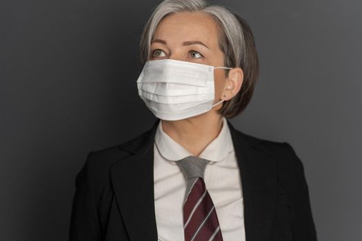 Gray-haired mid aged business woman in protective mask looking up. Selective focus on mask on female face. Virus outbreak concept.