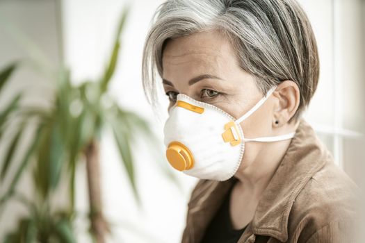 Side view of Mature woman in protective fp1 mask looking at side while leaning back against the window. Close up portrait. Tinted image.