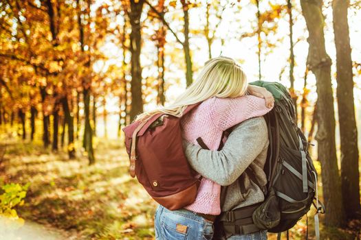 Embrace of couple of travelers, Man and woman with backpacks hugging while standing in the autumn forest. Copy space at left side.