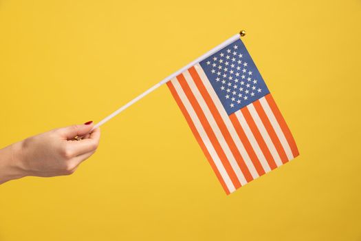 Profile side view closeup of human hand holding USA national flag. United states of America. National independance day - 4th july. Indoor studio shot isolated on yellow background.