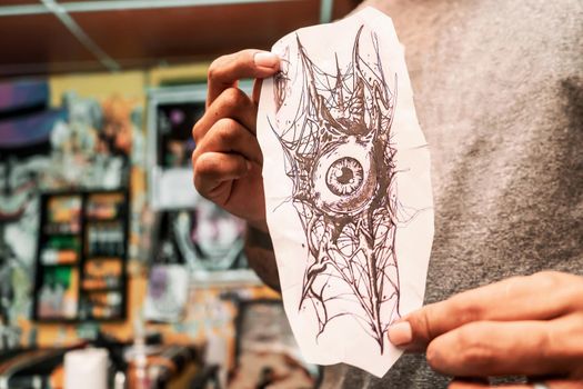 Unrecognizable Latino tattoo artist showing the sketch he drew to a client