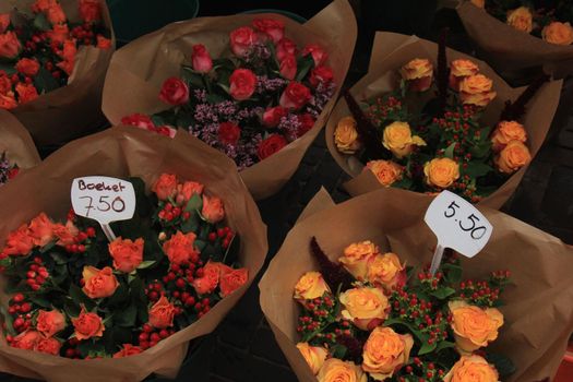 Bouquets with roses and berries in various colors at a market (text on tags: prices for a bouquet in euros, in Dutch)
