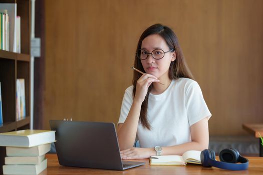 Back to school concept. Young college woman using laptop at library.