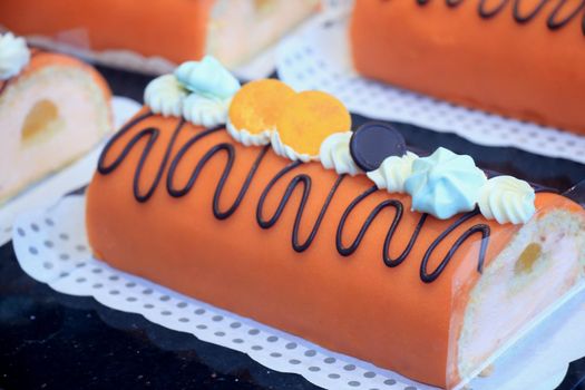 Orange marzipan confectionery, filled with cream and decorated with chocolate, on display in a shop