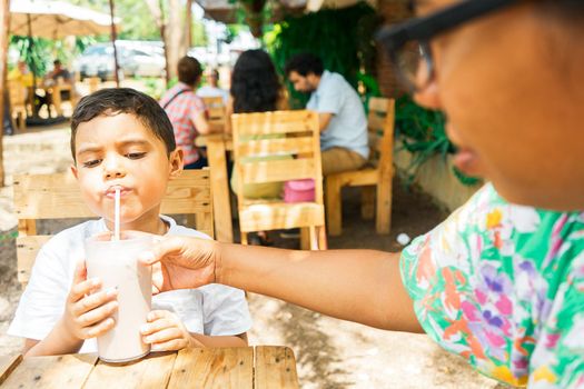 Latin mother giving her son a milkshake to drink in a country restaurant in Managua Nicaragua