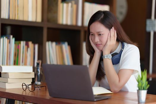 Back to school concept. Young college woman using laptop at library.