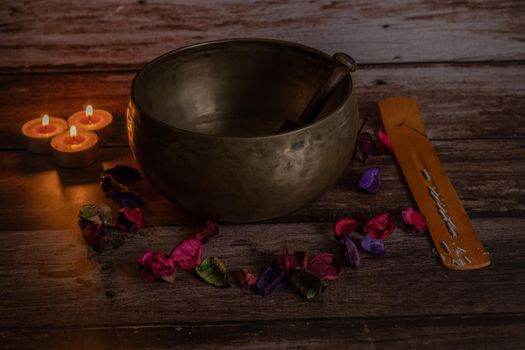 handmade tibetan bowl with flower petals and candles in dim light