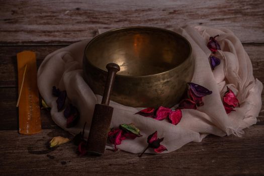 handmade tibetan bowl with flower petals and candles in dim light