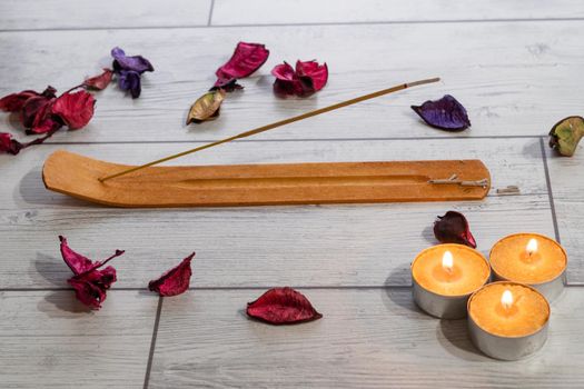 lighted incense stick on its stand with candles and flower petals on a white background and copy-space