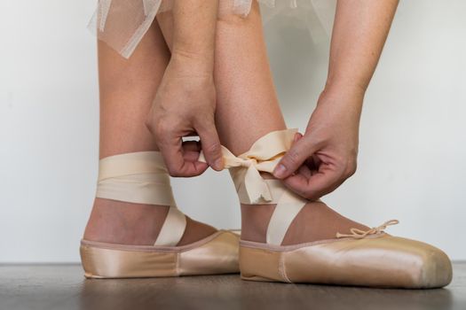 legs of girl dancing ballet with tulle skirt and pink shoes different dance steps wooden floor and white background with copy space