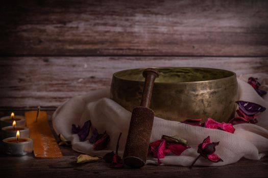 handmade tibetan bowl with flower petals and candles in dim light