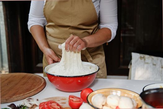 Artisanal bakery. Close-up Artisan chef hands kneading yeast dough in rustic wooden kitchen. Preparing delicious vegetarian Italian pizza or whole grain bread. Fresh ingredients are on kitchen couter