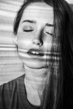 Closeup portrait of attractive woman with natural makeup posing with closed eyes, having dreamy expression. Black and white photography, indoor studio shot illuminated by sunlight from window.