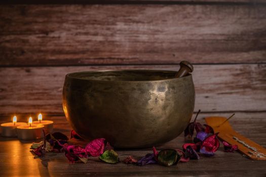 handmade tibetan bowl with flower petals and candles in dim light