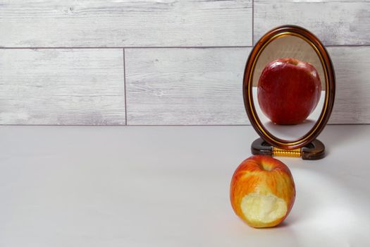 bitten red apple reflected in a mirror isolated on a white table with copy space