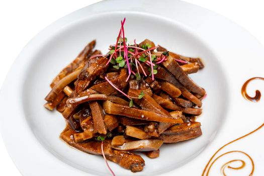 Fried pieces of pork in sauce decorated with microgreens. Marinated pig ears.