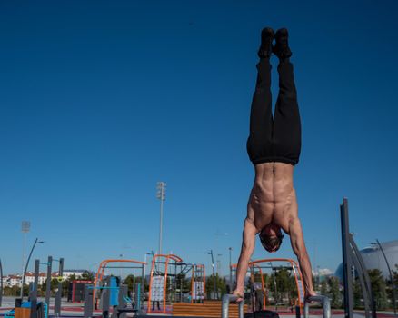 Shirtless man doing handstand on parallel bars at sports ground