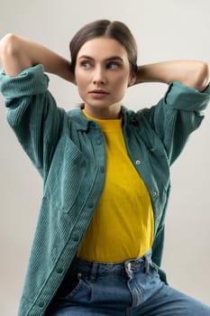 Portrait of perfect young adult woman with dark hair, emotion and feeling concept, sitting with raised arms, wearing casual style jacket. Indoor studio shot isolated on gray background.