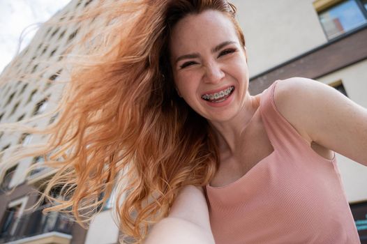 Beautiful young red-haired woman with braces on her teeth smiling in the summer outdoors.