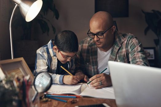 Keeping his little ones education going despite the lockdown. an adorable little boy completing a school assignment with his father at home