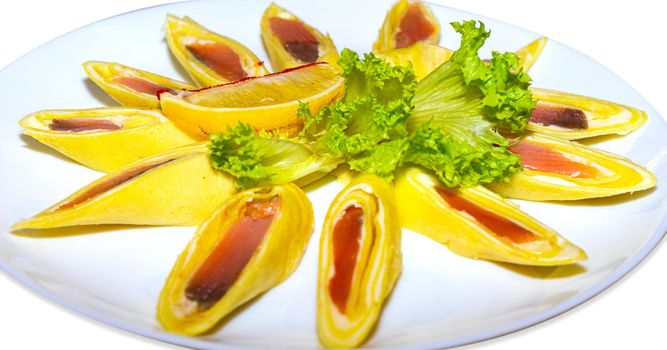 Pancakes stuffed with red fish and cut into pieces. Isolated plate with pancakes close-up.