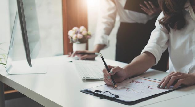 Close up Businesswoman hand holding pen and pointing at financial paperwork, financial charts to analyze profit concept.