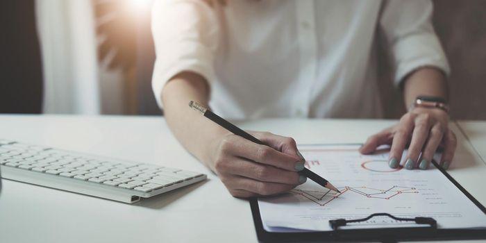 Close up Businessman hand holding pen and pointing at financial paperwork, financial charts to analyze profit concept.