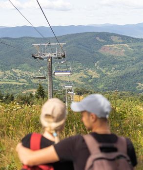 Man and a woman riding on the lift down the scenic Mountain during summer. Green tree forest surrounds the escalator