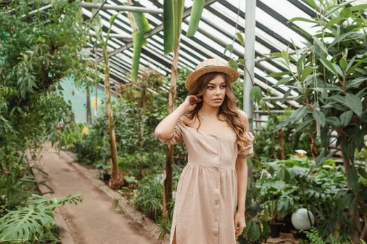 A beautiful young woman takes care of plants in a greenhouse. The concept of gardening and an eco-friendly lifestyle.