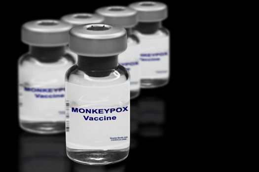Monkeypox vaccine close-up on a black mirror background. In the background are blurred vaccine vials..