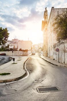 Beautiful architecture of an old streets decorated with plants in flowerpots. Bright sunset. Downtown, white city Ostuni, Bari, Italy. Tourism, travel concept.