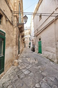 Beautiful architecture of an old streets decorated with plants in flowerpots and lights. Downtown, white city Ostuni, Bari, Italy. Tourism, travel concept.