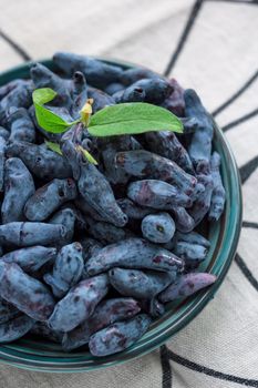 Closeup fresh blue honeysuckle or haskap berry on plate on fabric napkin, summer fruit, environmentally friendly natural organic healthy concept eco food, top view, vertical image, selective focus