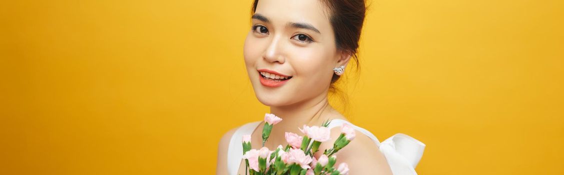 Portrait of a pretty young woman holding bouquet of carnation isolated over yellow background