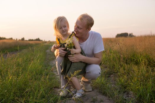 Dad and his blonde daughter are walking and having fun in a chamomile field. The concept of Father's Day, family and nature walks.