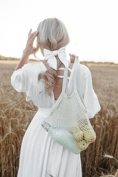 A blonde woman in a long white dress walks in a wheat field. The concept of a wedding and walking in nature.