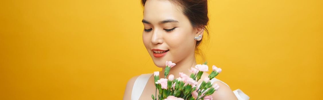 Portrait of a pretty young woman holding bouquet of carnation isolated over yellow background