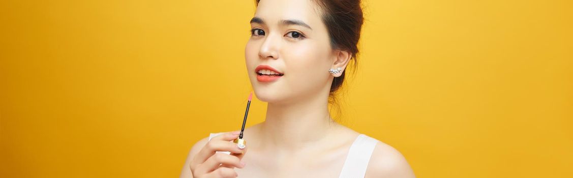Perfect girl holding lipstick on yellow background, close up portrait.