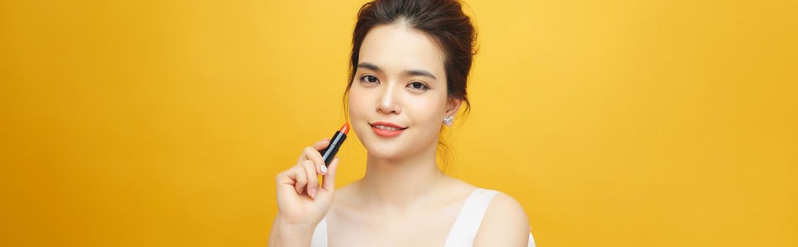 Beautiful asian woman holding red lipgloss on yellow background