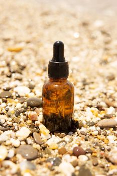 Cosmetic serum for the skin in a glass bottle. A bottle with an eyedropper on a pebble beach by the sea. Essences for skin care on the background of stones. The concept of natural cosmetics and SPA products.