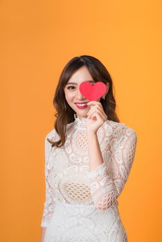 Portrait of young beautiful asian woman hands holding red heart shape isolated on yellow background.