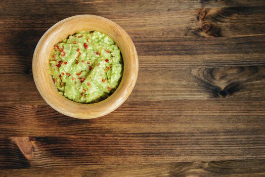 homemade guacamole with nachos in a wood bowl on a wooden table, typical mexican healthy vegan cuisine, top view and copy space for text