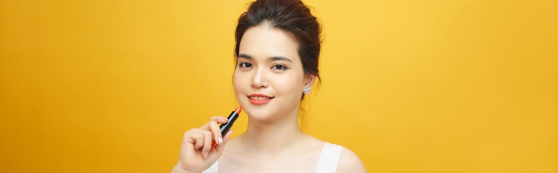 Beautiful asian woman holding red lipgloss on yellow background