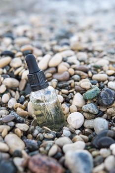 Cosmetic serum for the skin in a glass bottle. A bottle with an eyedropper on a pebble beach by the sea. Essences for skin care on the background of stones. The concept of natural cosmetics and SPA products.