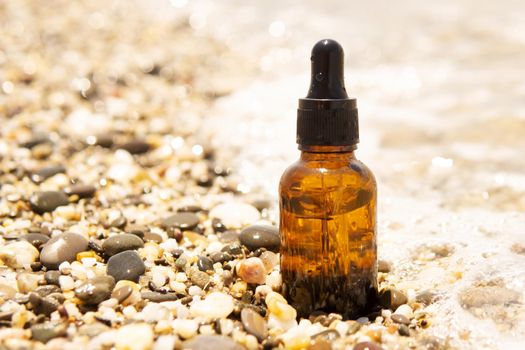 Cosmetic serum for the skin in a glass bottle. A bottle with an eyedropper on a pebble beach by the sea. Essences for skin care on the background of stones. The concept of natural cosmetics and SPA products.