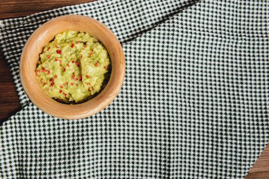 homemade guacamole in a wood bowl and a kitchen rag on a wooden table, typical mexican healthy vegan cuisine, top view and copy space for text