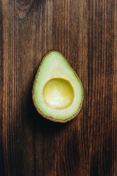 top view of half avocado without seed on wooden table, healthy vegan cuisine concept with rustic dark food photo style, vertical photo