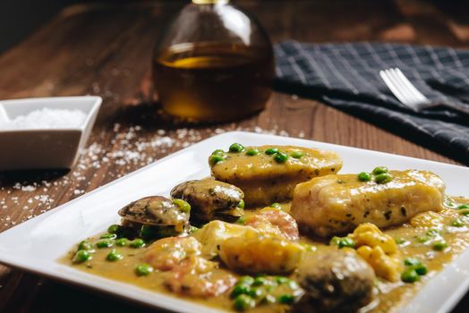 healthy traditional spanish hake dish with green seafood sauce with clams, prawns, green peas and egg, typical mediterranean cuisine with rustic dark food photo style