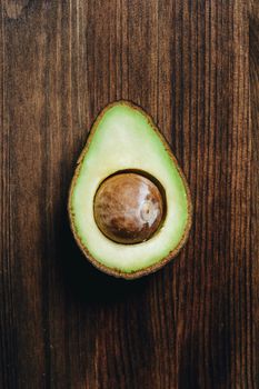 top view of half avocado with bone on wooden table, healthy vegan cuisine concept with rustic dark food photo style, vertical photo